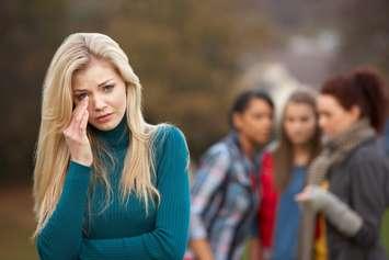Upset teenage girl with friends in background. Photo courtesy of @monkeybusiness CanStock.