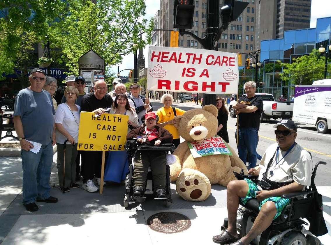 Hamilton Health Coalition volunteers join OHC executive director Natalie Mehra in downtown Hamilton with the giant teddy bear. (Photo courtesy of the Ontario Health Coalition)