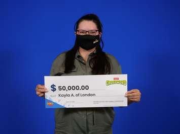 Kayla Albert of London smiles under her face mask while holding a $50K cheque for winning on a Crossword scratch ticket. Photo via OLG Communications. 