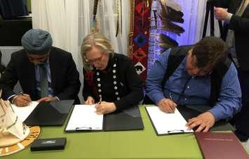From left to right:  Harjit Sajjan, Carolyn Bennett and Tom Bressette sign the agreement for the return of the former Camp Ipperwash April 14, 2016 (BlackburnNews.com photo by Briana Carnegie)