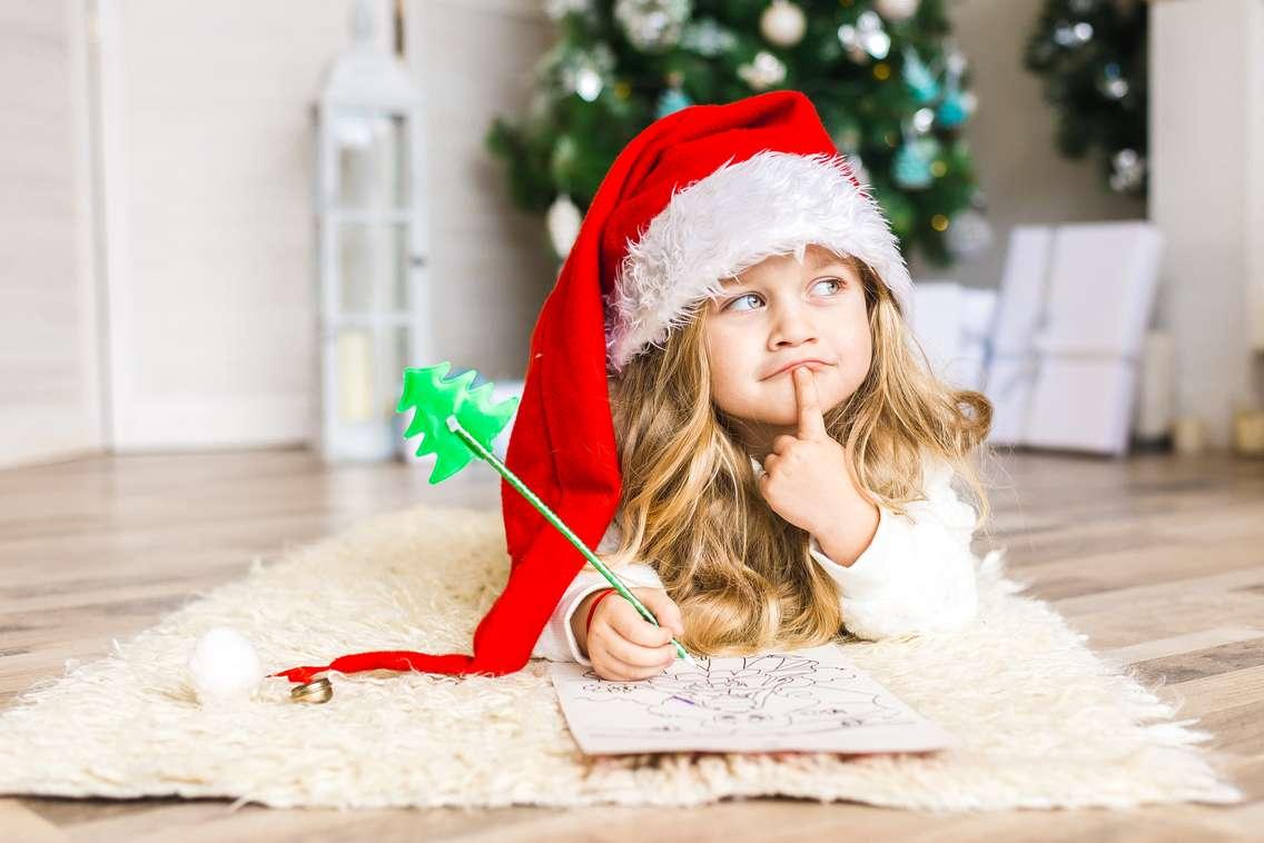 Little girl in Santa hat writes letter to Santa Claus. Photo by Lakshmi3 / iStock / Getty Images Plus via. Getty Images