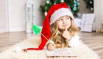 Little girl in Santa hat writes letter to Santa Claus. Photo by Lakshmi3 / iStock / Getty Images Plus via. Getty Images