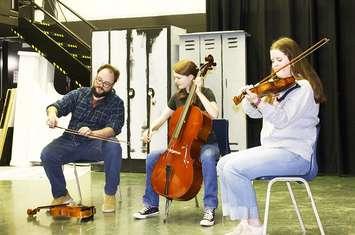Cam Bowman demonstrating bowing to Hannah Hewitt (Cello) and Jalyssa Martin (violin). Photo provided by Banding Together.