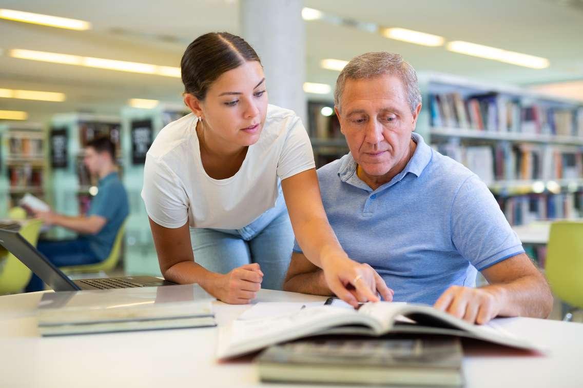 Young woman explaining information to a mature man in the library. Photo by JackF / iStock / Getty Images Plus via Getty Images.