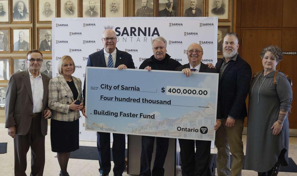 Cheque presentation at Sarnia City Hall. (from left to right) City/County Councillor Dave Boushy, City Councillor Anne Marie Gillis, Associate Minister of Housing Rob Flack, Mayor Mike Bradley, MPP Bob Bailey, City/County Councillor Brian White, and City/County Councillor Chrissy McRoberts. March 13, 2024. (Photo by Natalia Vega)