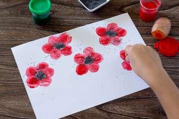 A child paints poppies on a piece of paper. elena_hramowa / iStock / Getty Images Plus via Getty Images