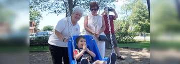 Youngster Nolan takes a ride in a Jenn Swing while Donna Clendenning (left) and Point Edward Mayor Bev Hand (right) give him a push. June 25, 2019. (BlackburnNews photo by Colin Gowdy)