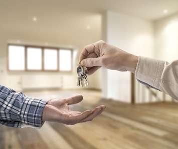 Realtor handing over keys to a house in an empty room. © Can Stock Photo / pbombaert