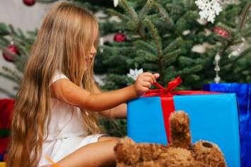 A young child opening a Christmas present. © Can Stock Photo / Kzenon