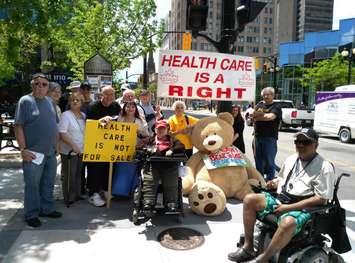 Hamilton Health Coalition volunteers join OHC executive director Natalie Mehra in downtown Hamilton with the giant teddy bear. (Photo courtesy of the Ontario Health Coalition)