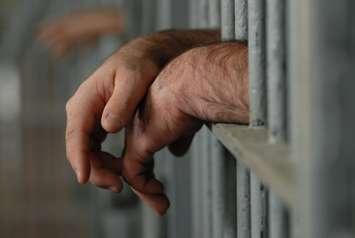 Man's hands behind bars in jail or prison.  © Can Stock Photo Colecanstock.