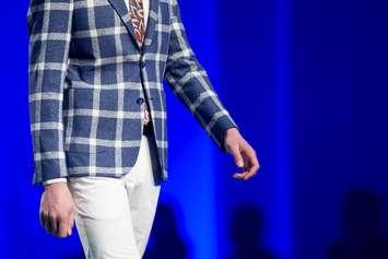 A male model walks the runway in modern blue suit with white trousers during a fashion show. fashion catwalk event showing new collection of clothes. blue background. © Can Stock Photo / Belish